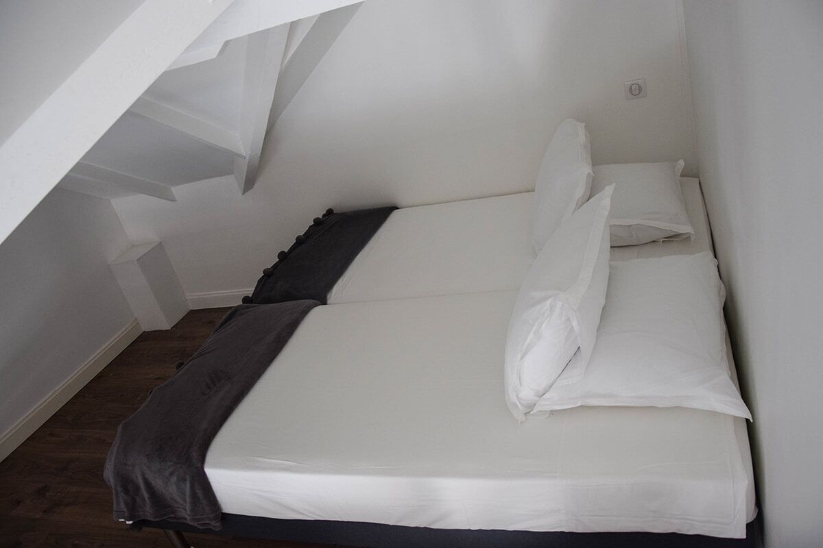 Ein kleines Zimmer mit einem Einzelbett, weißer Bettwäsche und einem dunkel gefärbten Kopfteil.
