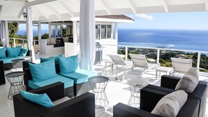Un espacio de estar techado al aire libre con mobiliario de mimbre y cojines, con vistas a un paisaje marino.