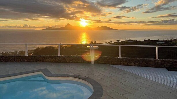 Una piscina con vista a la puesta de sol sobre el océano.