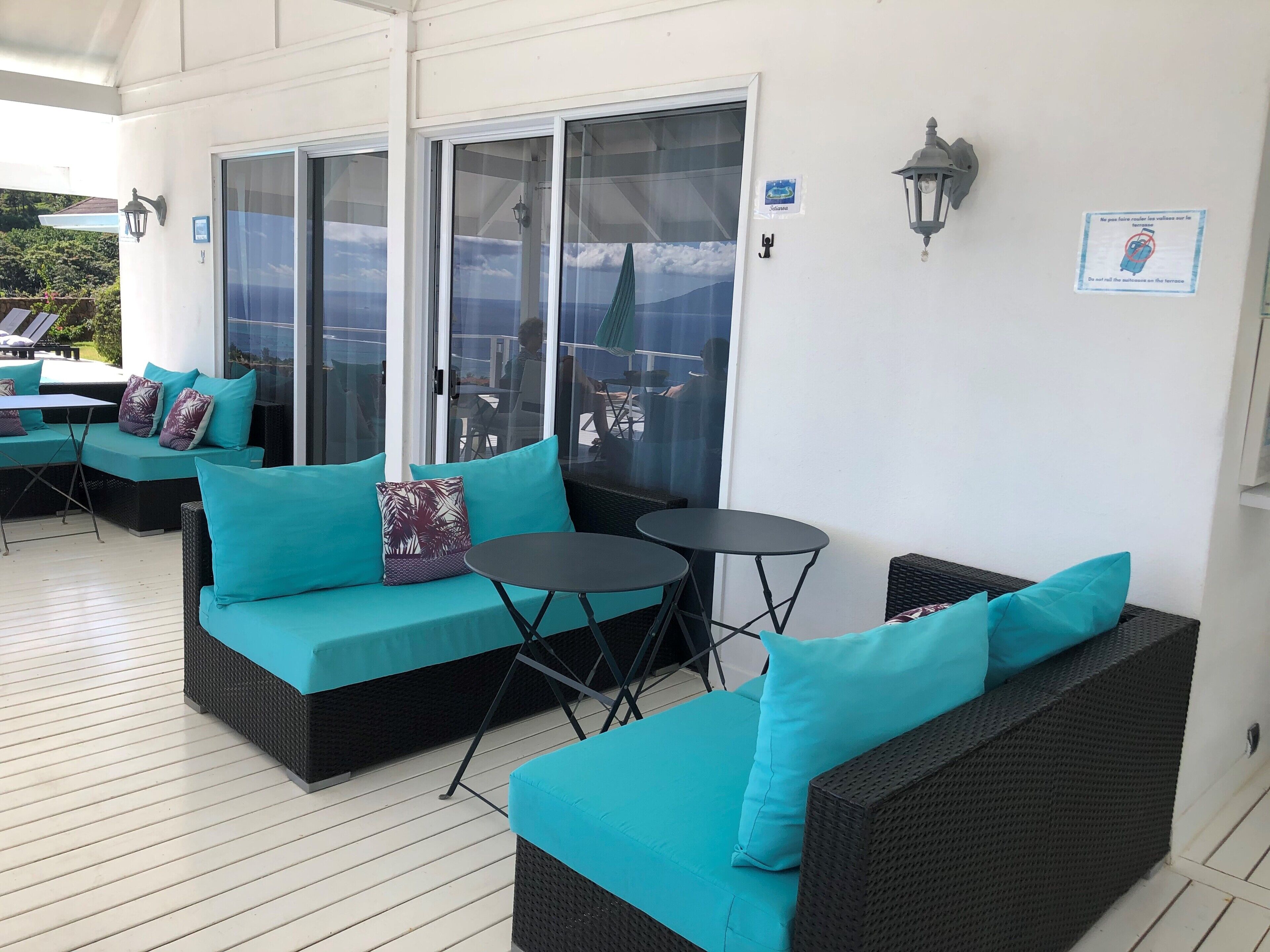 A covered outdoor seating area with teal cushions and wicker furniture, featuring a glass door leading to an outdoor patio.