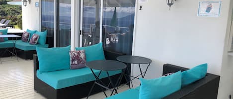 A covered outdoor seating area with teal cushions and wicker furniture, featuring a glass door leading to an outdoor patio.