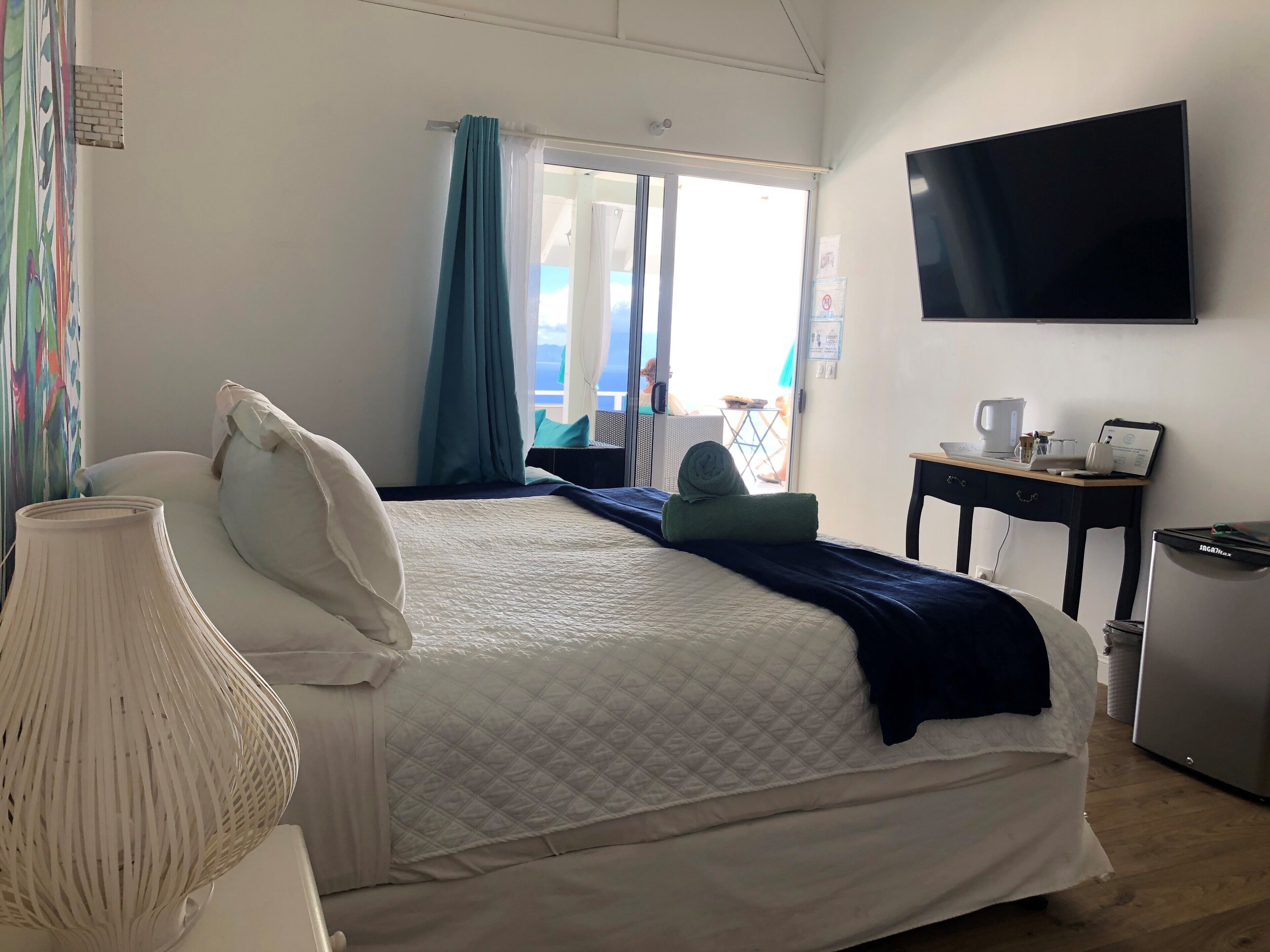 A hotel room with a bed, a desk with a computer, a TV, and a view of the outdoors.
