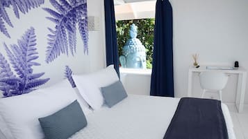 A bedroom with a bed, a window with a view of greenery, a white desk, and a chair.