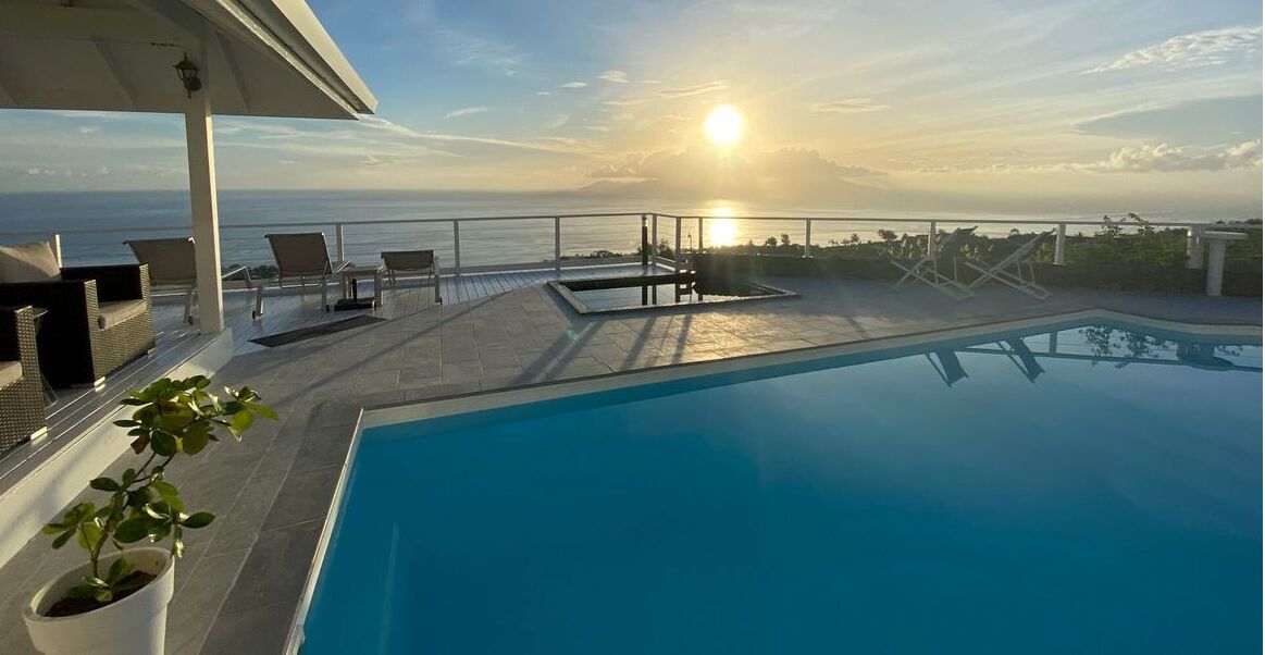 Una piscina en la azotea con sillones de descanso y vistas al océano al atardecer.