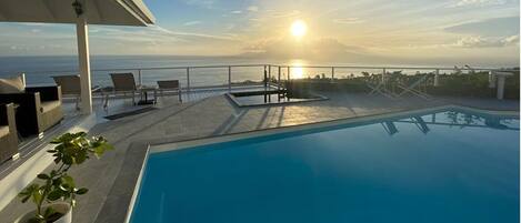 A rooftop pool with lounge chairs and a view of the ocean at sunset.