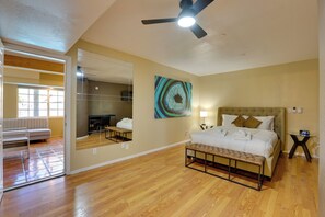 A hotel room with a bed, bench, ceiling fan, artwork, and a mirror.