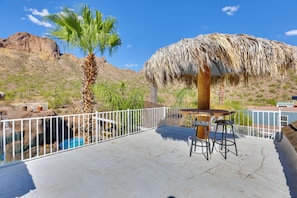 A poolside area with a thatched umbrella, a palm tree, and a mountain backdrop.
