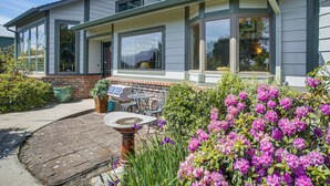 A house with large windows, a patio with outdoor furniture, and a garden with flowers. - Unique Home w/ Beautiful Mtn Views! (Sequim)