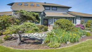 A two-story house with a sloped roof, a front porch, and a landscaped garden with various plants and a small tree. - Unique Home w/ Beautiful Mtn Views! (Sequim)