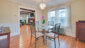 Uma sala de jantar com uma mesa redonda, quatro cadeiras, um candelabro e uma orquídea em vaso.