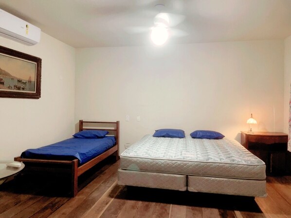 A small, single-room accommodation with a bed, a bedside table, and a nightstand. - Beach House Unid. 3 Casas Praia Guarujá (Guarujá)