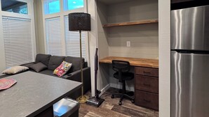 Een compacte keuken met houten plafond, een inbouwkoelkast, een eethoek met een bankje en een werkplek met bureau en stoel.