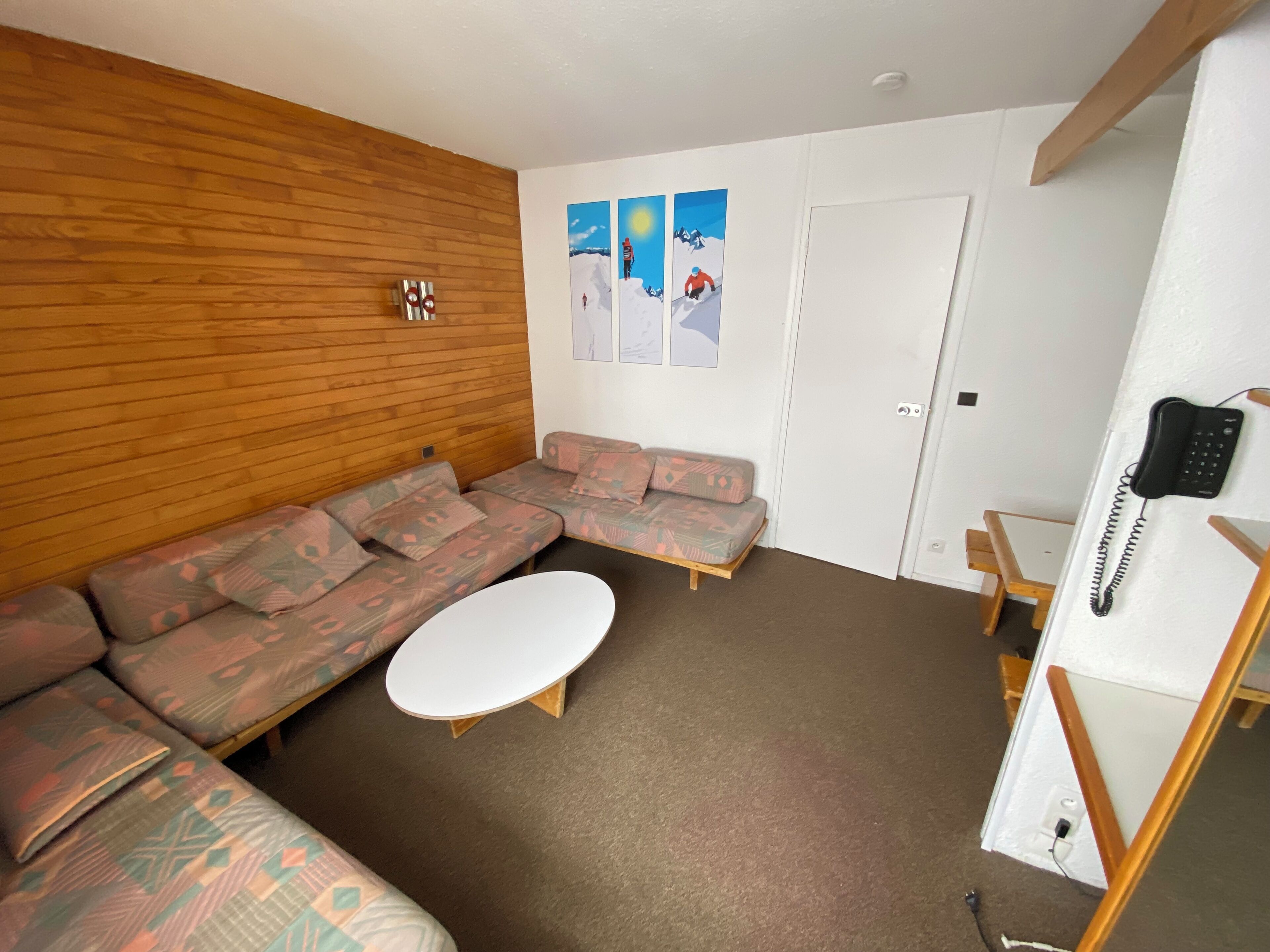 Ein Zimmer mit einer Holzwand, einem Ecksofa, einem weißen Couchtisch und einer Tür mit einem Telefon.