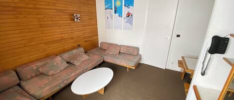 Ein Zimmer mit einer Holzwand, einem Ecksofa, einem weißen Couchtisch und einer Tür mit einem Telefon.