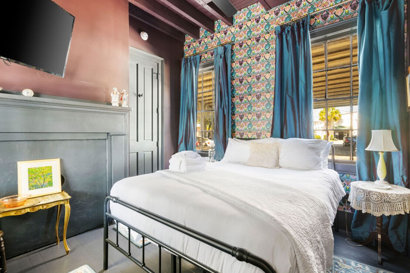 Quarto com cama, mesa de cabeceira, luminária e janela com cortinas.