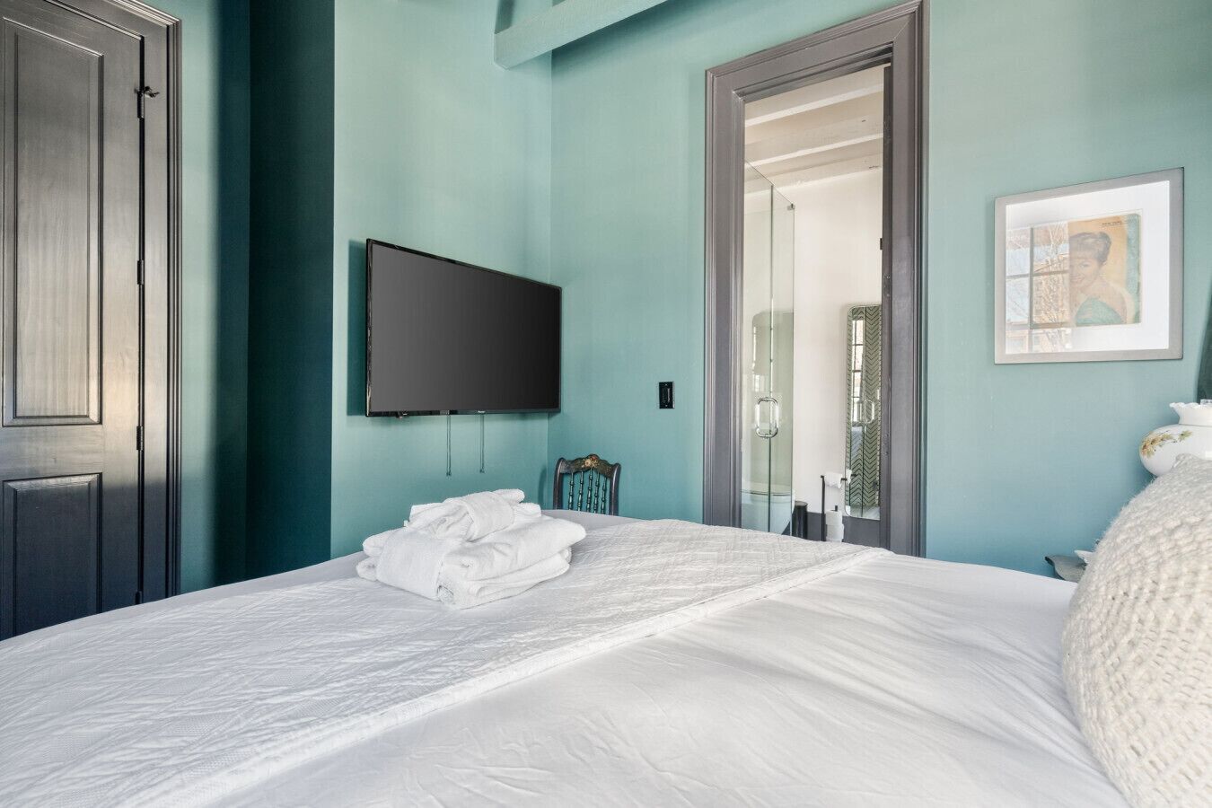 A bedroom with a bed, a flat-screen TV, a door, and a framed picture on the wall.