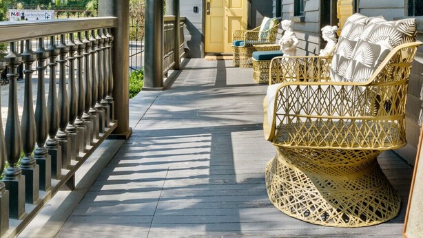 Une véranda couverte avec une balustrade, des meubles en osier et une porte jaune.