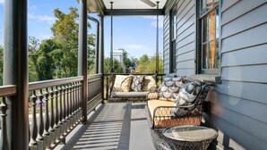 Eine überdachte Veranda mit einer Couch und Stühlen, einem Deckenventilator und Blick auf ein Haus im Hintergrund.
