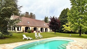 Ein Swimmingpool mit Ziegelbordura, umgeben von Rasen und Bäumen.