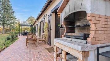 Eine Terrasse im Freien mit rotem Ziegelboden, Holzmöbeln und einem Backofen aus Ziegeln.