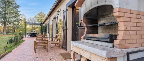 Eine Terrasse im Freien mit rotem Ziegelboden, Holzmöbeln und einem Backofen aus Ziegeln.