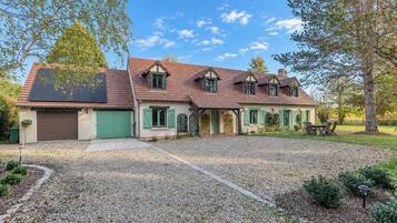 Een twee verdiepingen tellend huis met een grindpad, groene luiken en een zonnepaneel op het dak.