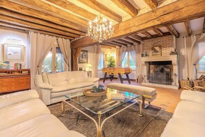A spacious living room with a fireplace, wooden beams, and a glass coffee table.