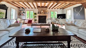 Ein rustikales Wohnzimmer mit freiliegenden Holzbalken, einem Kamin, einem Fernseher und zwei weißen Sofas.