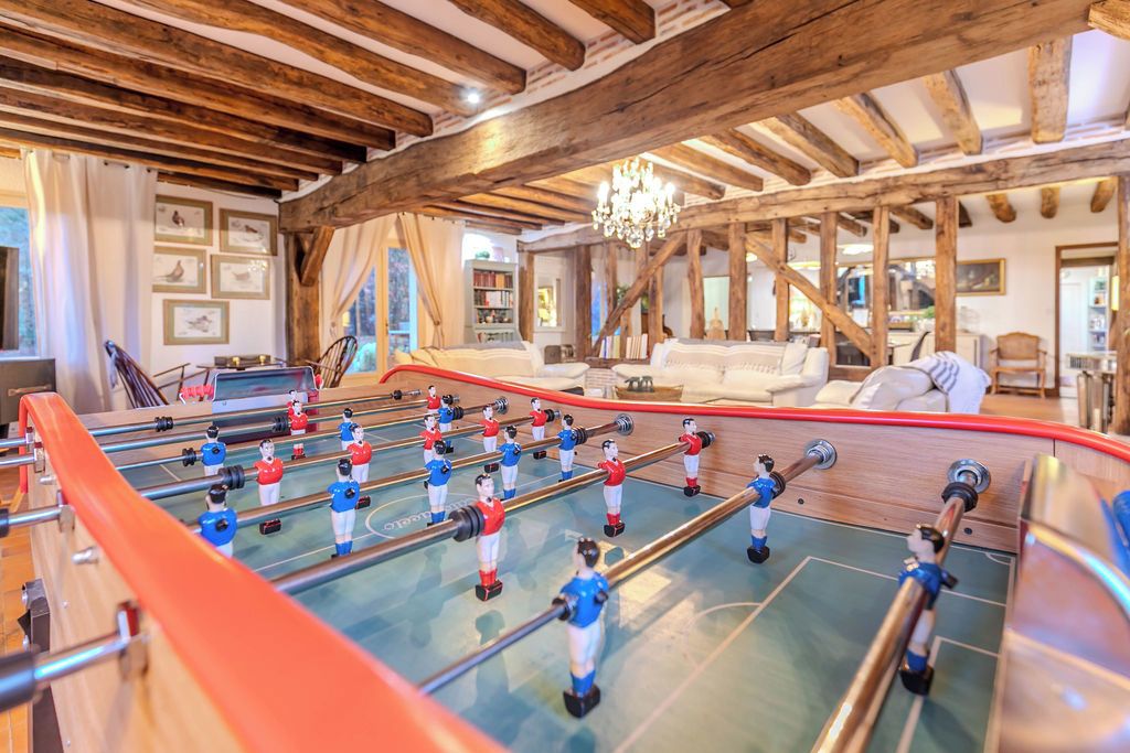 Een kamer met een tafelvoetbaltafel, houten balken, een kroonluchter en een bank.