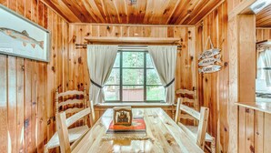 L’intérieur d’un chalet en bois, avec une table à manger, des chaises, une fenêtre avec des rideaux et un panneau accroché au mur.