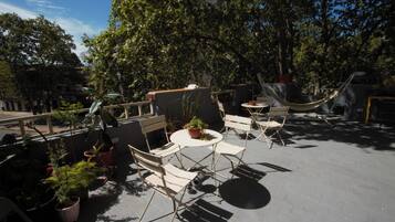 An outdoor patio with a round table and four chairs, surrounded by potted plants and a hammock.