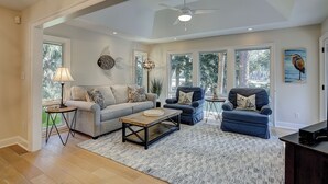 Un salon spacieux comprenant un canapé, des fauteuils, une table basse et un ventilateur de plafond.