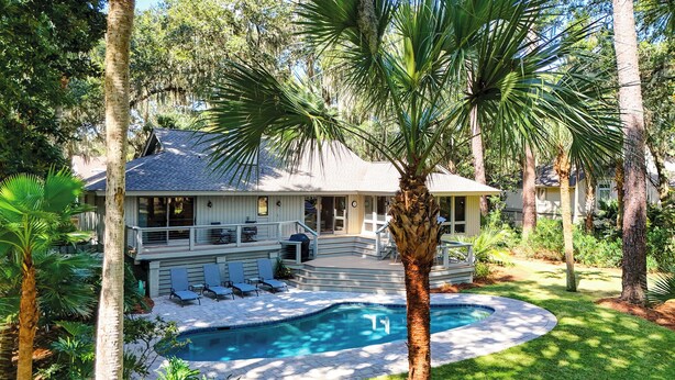 Une maison avec une piscine, entourée de palmiers et d’une pelouse bien entretenue.