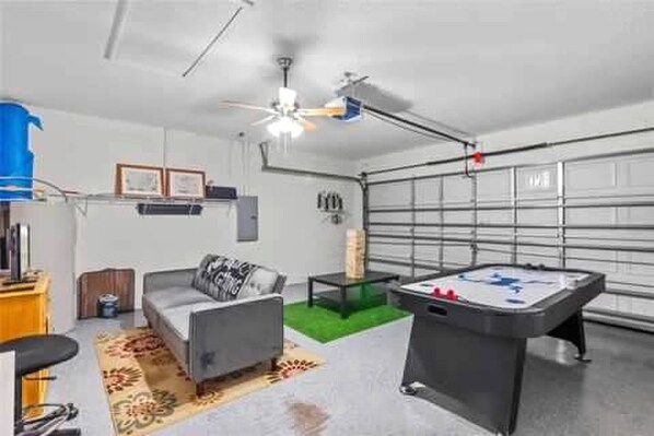 Une pièce avec une table de billard, un canapé, un ventilateur de plafond et une porte de garage.
