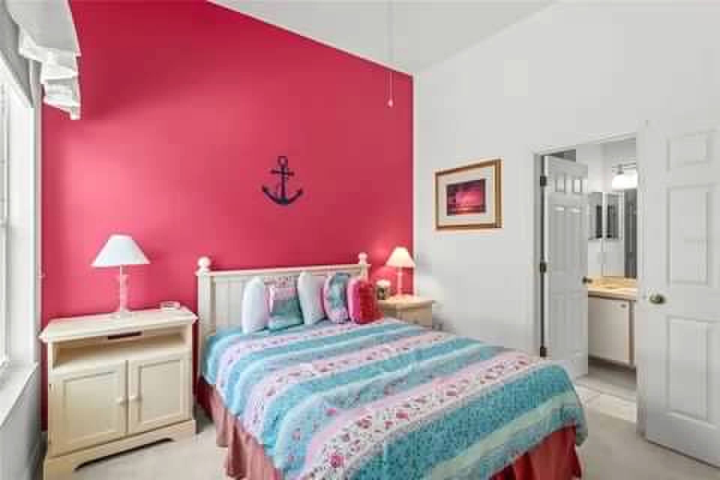 Une chambre avec un mur rose, un lit recouvert d’une couvre-lit à motifs floraux, deux tables de chevet avec des lampes et une porte donnant sur une autre pièce.