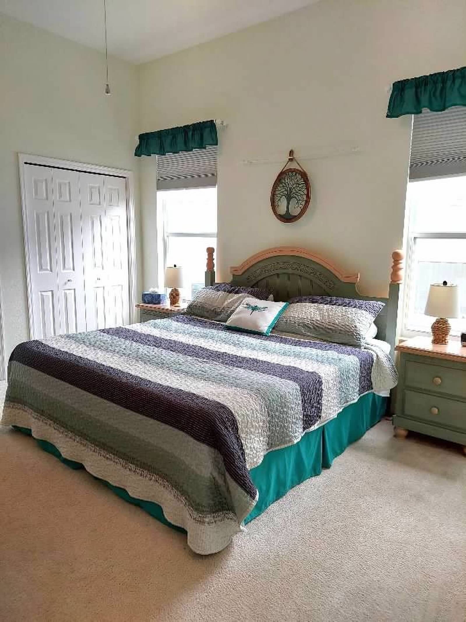 A bedroom with a large bed, two bedside tables, a door, and a window with curtains.