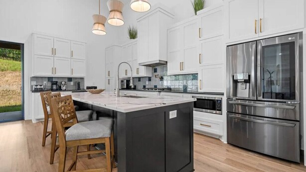 Une cuisine moderne avec des meubles blancs, un îlot central, des appareils en acier inoxydable et des luminaires suspendus.