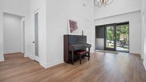 Une pièce spacieuse dotée d’un parquet, d’un piano, d’une grande fenêtre et d’un lustre.