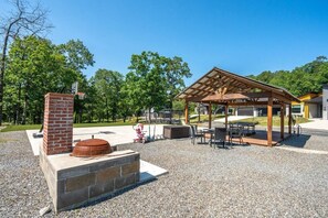 An outdoor patio area with a brick fireplace, a covered seating area, and a playground in the background.