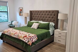 A neatly arranged bedroom with a tufted headboard, a floral bedspread, and two bedside tables with lamps.