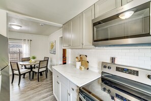 A modern kitchen with white cabinetry, a stainless steel microwave, an oven, and a dining area with a table and chairs.