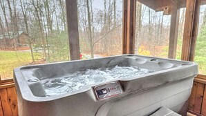 Een hottub met bedieningspaneel, een houten terras en uitzicht op bomen en een huis door grote ramen.
