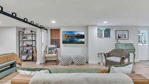 Un salon moderne avec un canapé, des poufs, une bibliothèque, un fauteuil et un tableau accroché au mur.