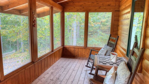 Eine Holzhütte mit Veranda, großen Fenstern und einer Sitzecke mit Stühlen und Kissen.