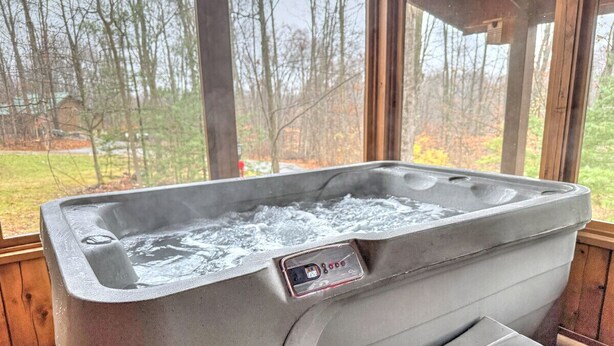 Un jacuzzi con panel de control, ubicado en una cabaña de madera con amplias ventanas que dan a un área boscosa.