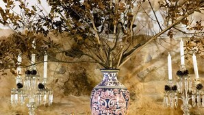 Un jarrón decorativo con diseños intrincados, flanqueado por dos candelabros con velas encendidas, sobre un muro con textura.