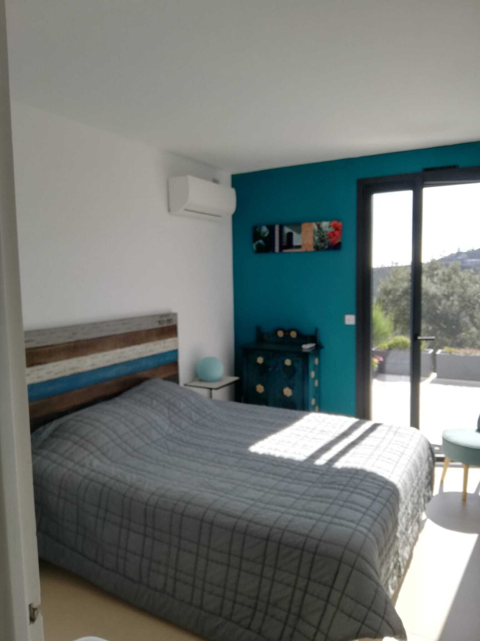 A bedroom with a bed, a dresser, a small table, and a window with a view of greenery.