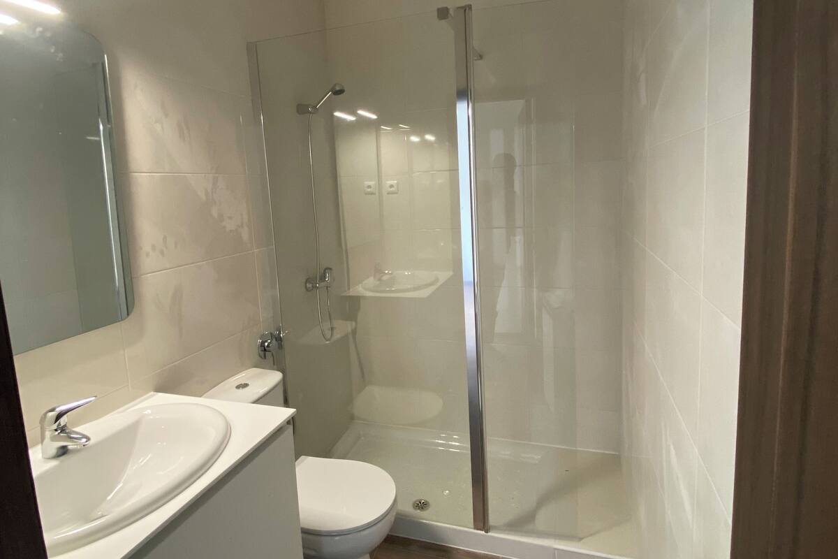 A modern bathroom with a glass-enclosed shower, a white sink, and a toilet.