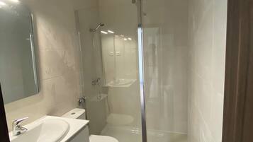 A modern bathroom with a glass-enclosed shower, a white sink, and a toilet.