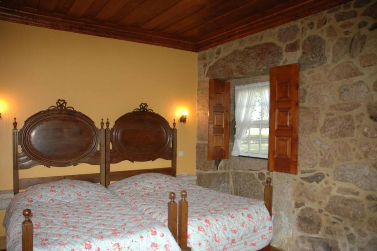 A bedroom with a double bed, wooden headboard, stone walls, and a window with wooden shutters.